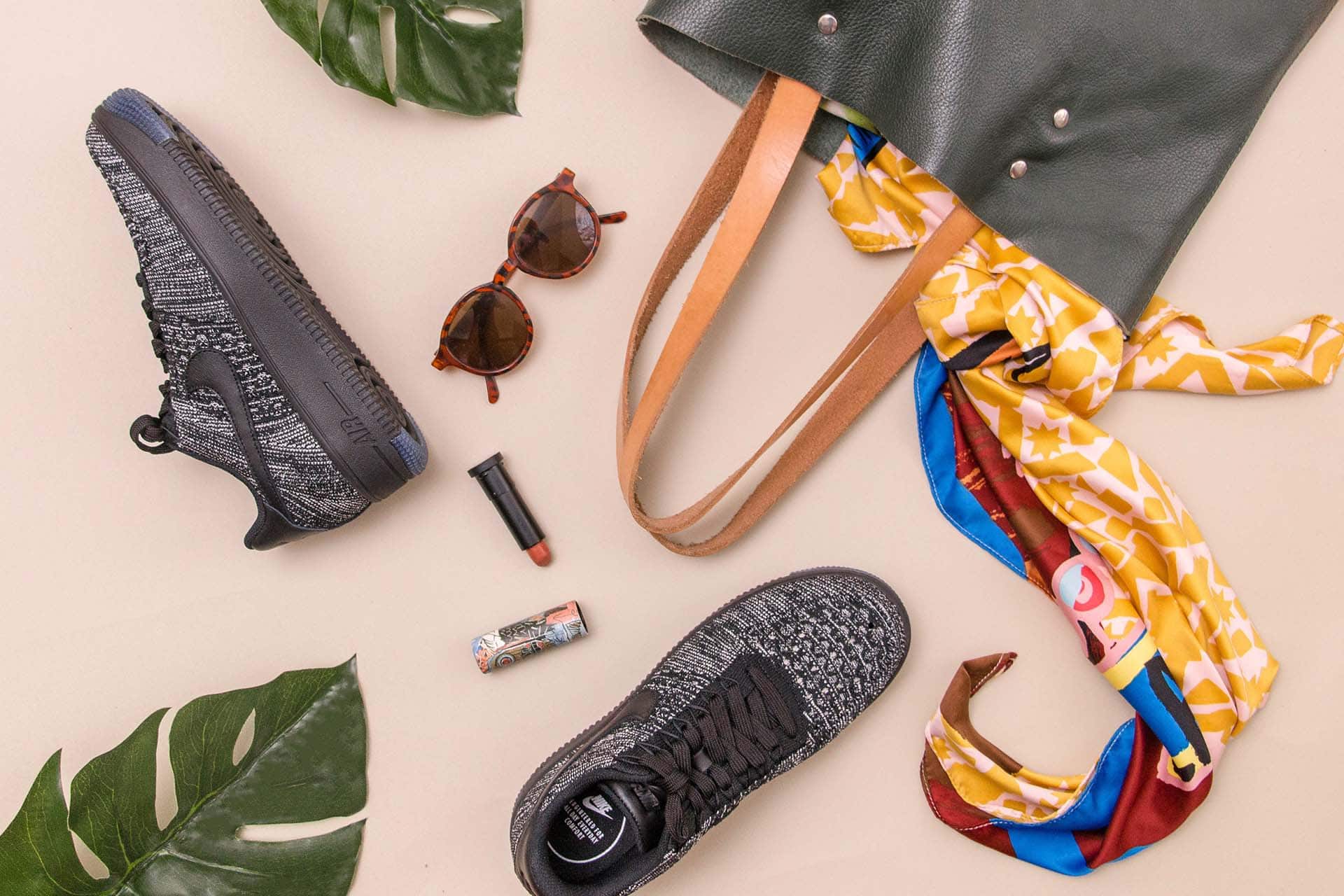 Flatlay of black bag, grey trainers, sunglasses, and lipstick
